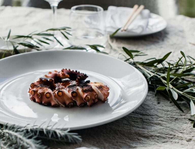 Elegant octopus dish elegantly plated on a gourmet table setting with chopsticks and wine.
